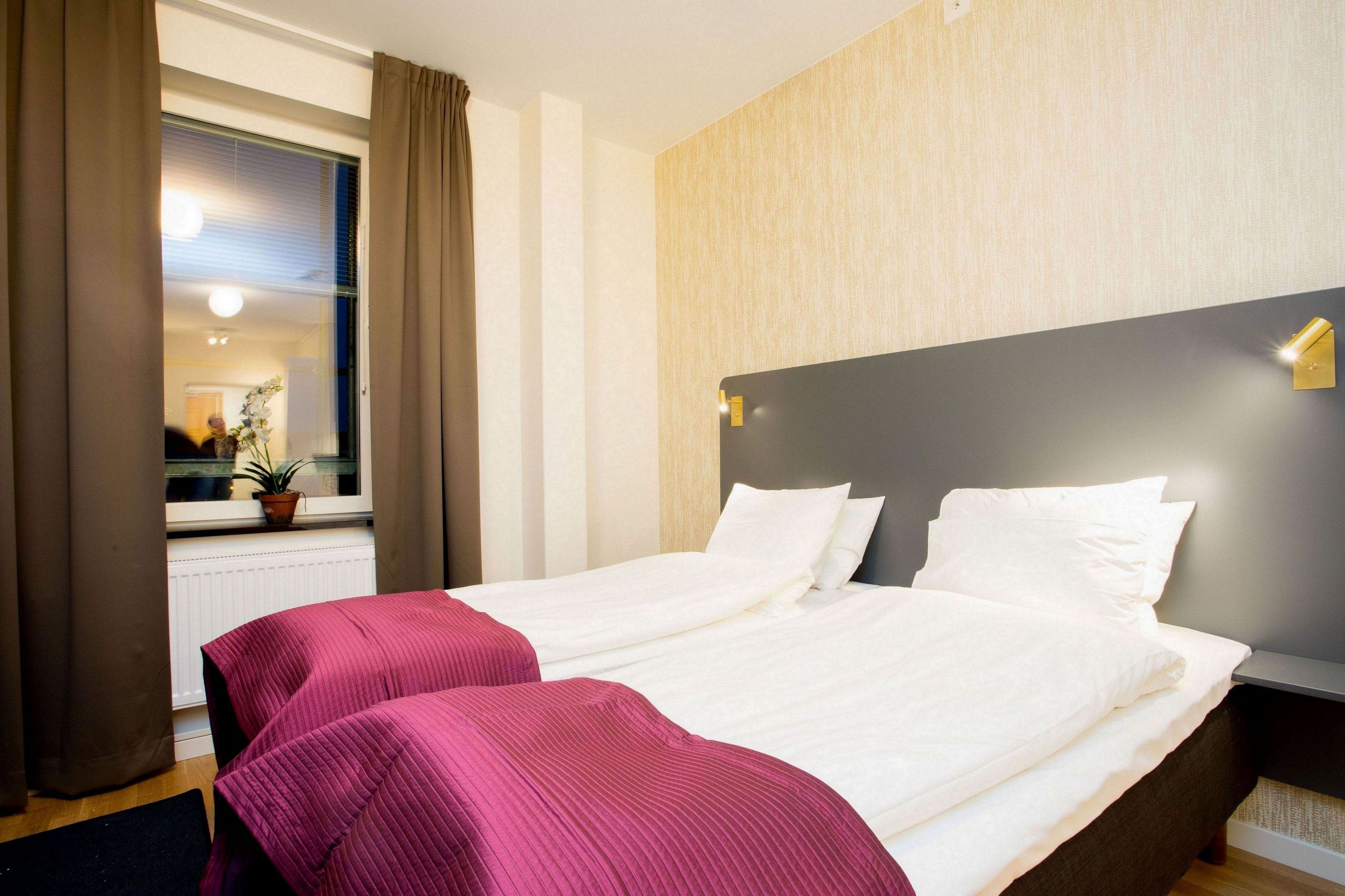 Habitación de hotel con una cama grande, una mesita de noche, una ventana con cortinas y vista al interior.