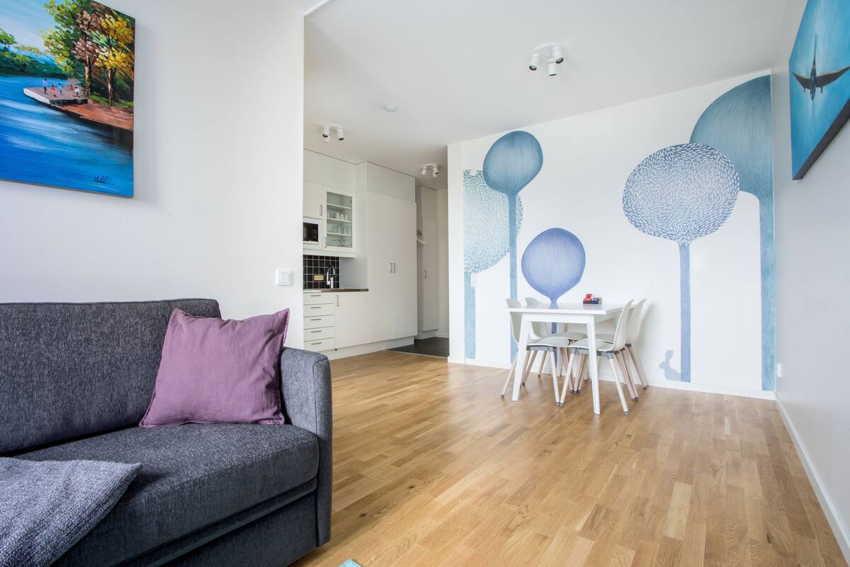 Una sala de estar moderna con un sofá gris, una mesa de comedor con sillas y una cocina al fondo.