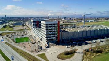 A large industrial building with multiple floors, a parking area, and a green field nearby.