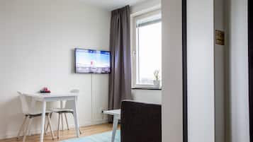 A modern room with a white desk, two chairs, a television mounted on the wall, a window with curtains, and a door with a sign.