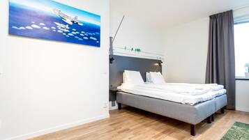 A modern bedroom with a grey bed, white bedding, a painting of an airplane, and a window with curtains.