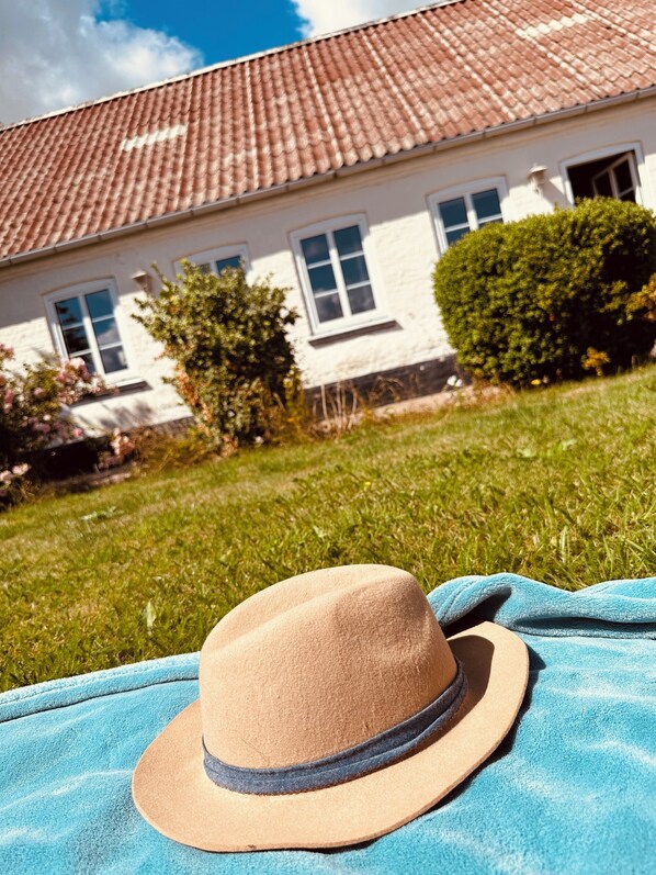 A hat on a blue towel in front of a house with a tiled roof and windows.