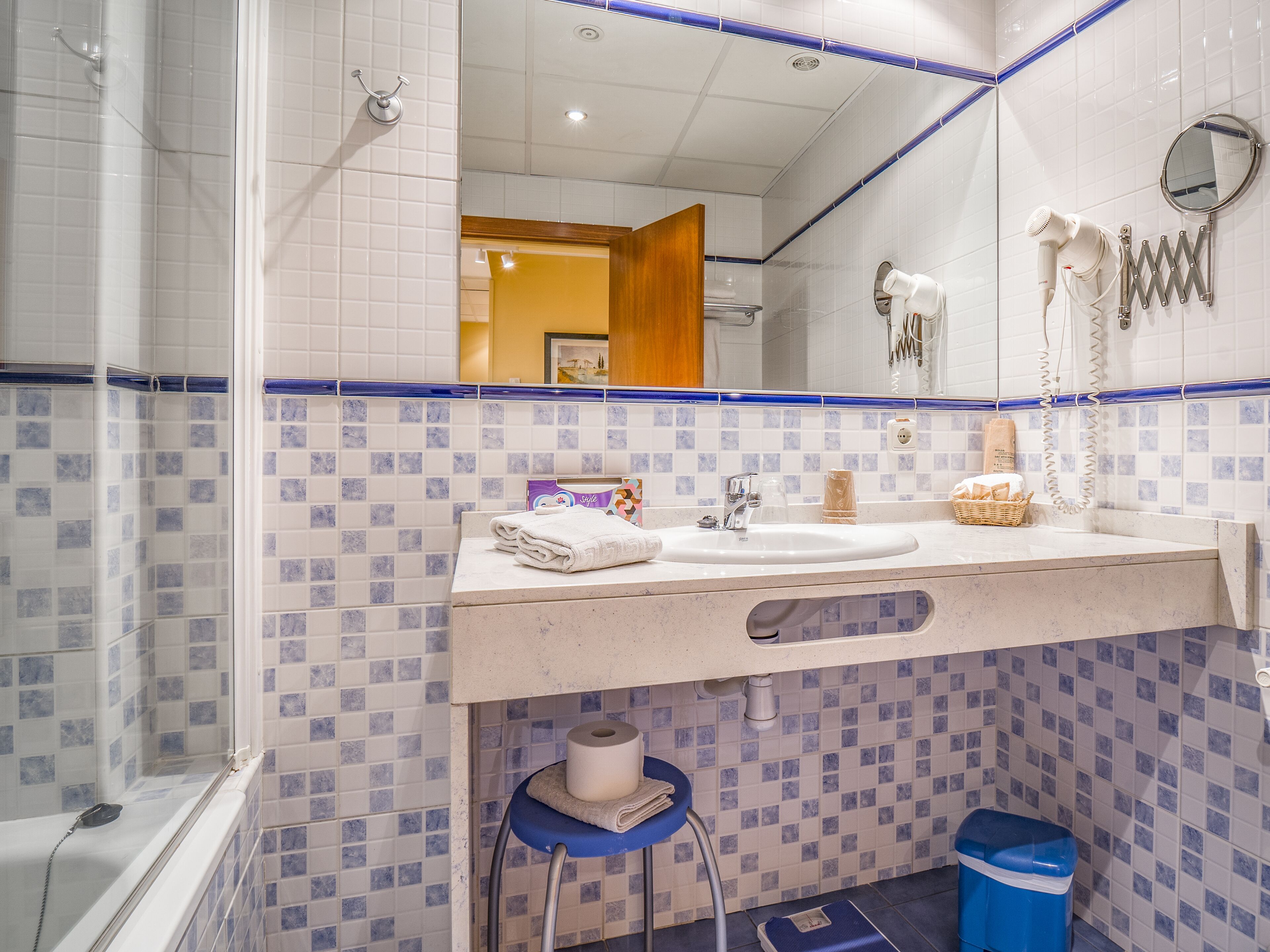 A bathroom with a sink, mirror, towel rack, and a blue trash bin.