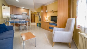 Un espacio habitable compacto con kitchenette, comedor y zona de estar con sofá y sillón.