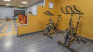 Un gimnasio con bicicletas estáticas, piso a cuadros y pared amarilla.
