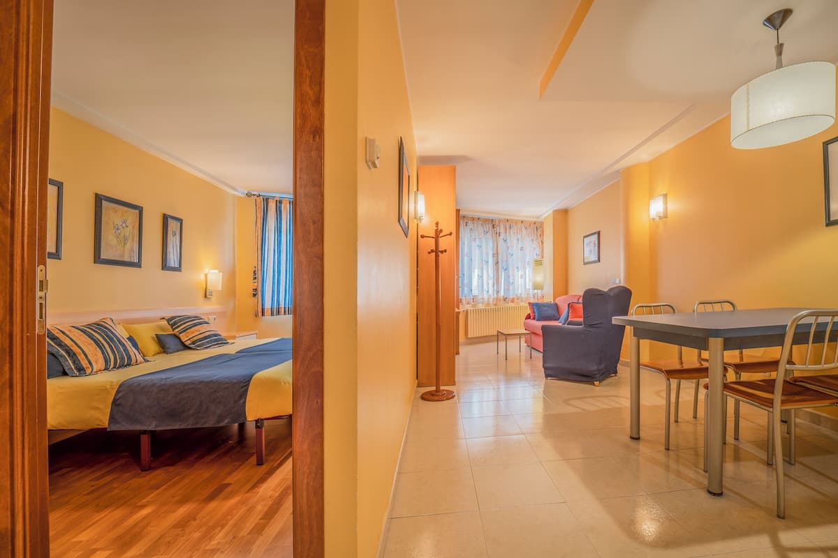 Une chambre d’hôtel avec un lit, une table et des chaises. Un couloir mène à une autre pièce.