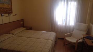 Habitación de hotel con dos camas, una silla, una mesita y un cuadro en la pared.