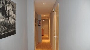 Un pasillo estrecho con suelo de madera, un extintor en la pared y una puerta a la derecha.