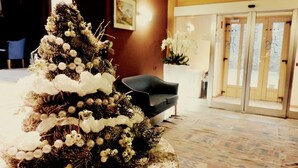 A Christmas tree with white decorations in a lobby area with a black sofa and a glass door entrance. - Residence Pizzo Scalino (Chiesa in Valmalenco)