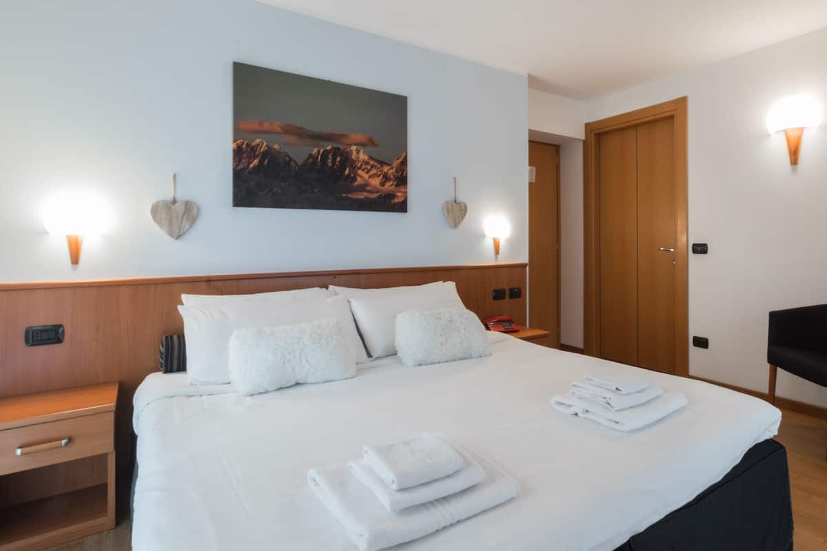 A hotel room with a large bed, a bedside table, a desk, a chair, and a painting on the wall.
