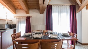A dining area with a wooden table set for four, surrounded by chairs. A microwave is visible on the counter to the left. - Residence Pizzo Scalino (Chiesa in Valmalenco)