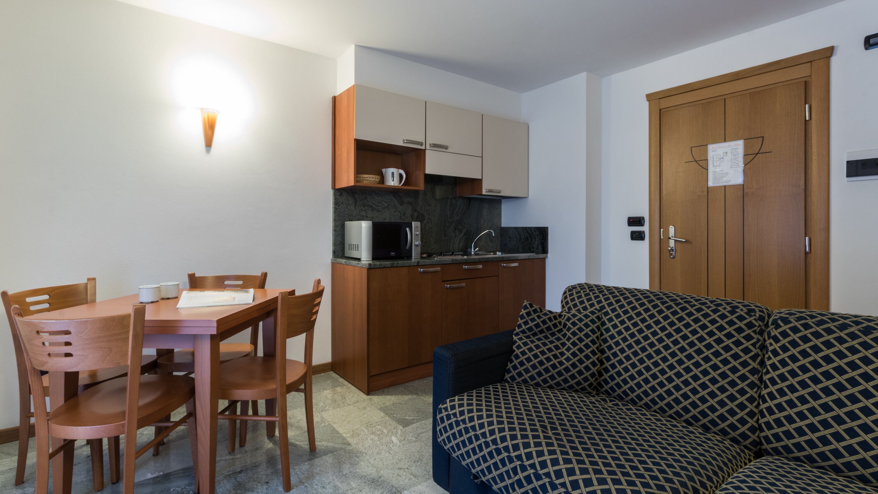 A compact living space with a dining table, chairs, a microwave, a sink, and a sofa.