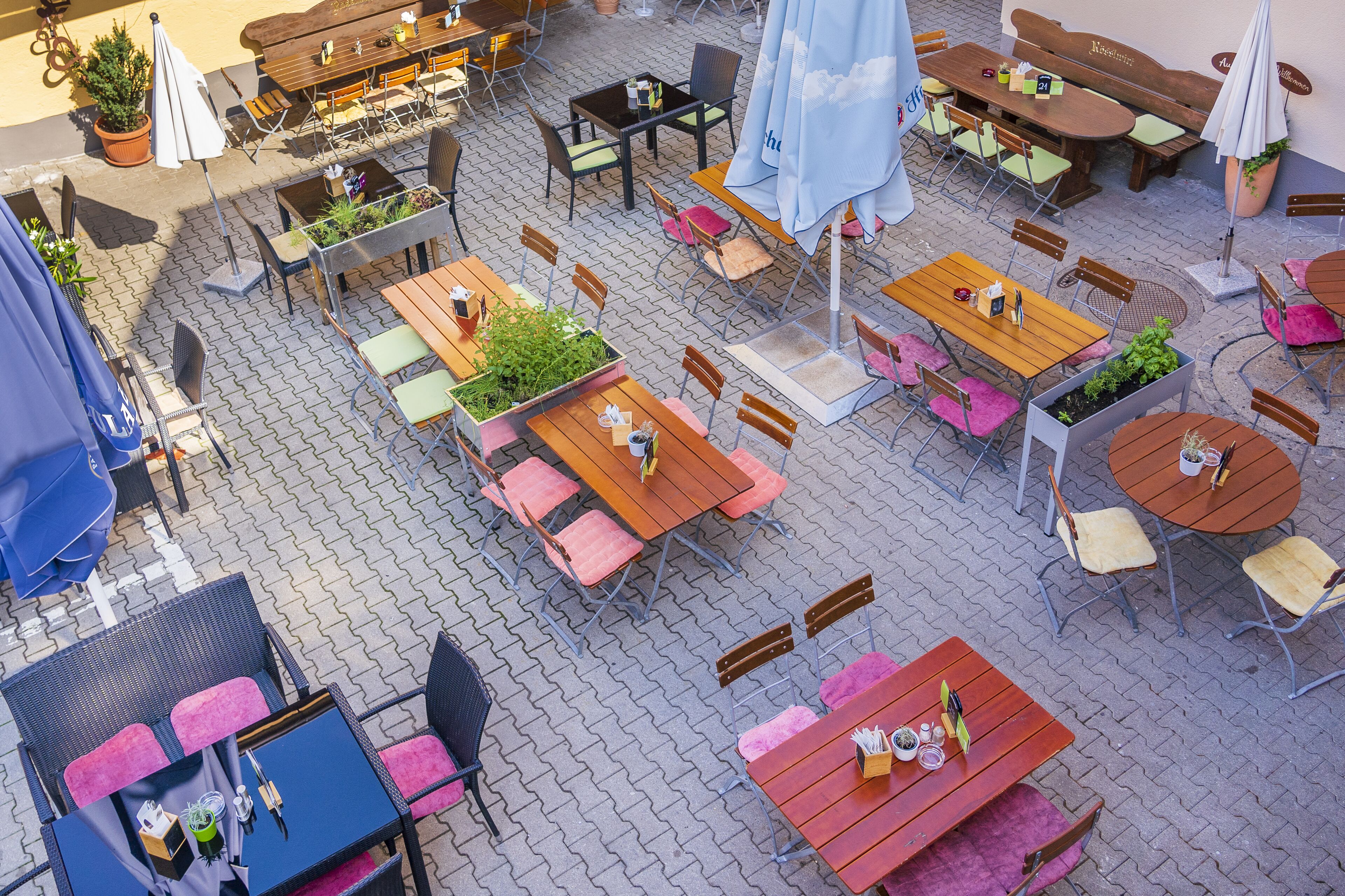 An outdoor café with multiple wooden tables and chairs, some with umbrellas.