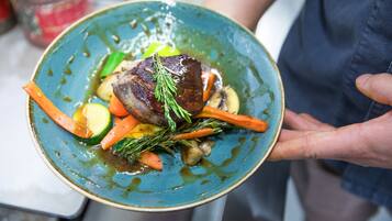 A person holding a plate with a piece of meat, vegetables, and a sprig of herb.