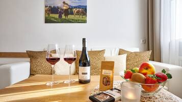 A dining table with a bottle of wine, two glasses, a candle, a fruit bowl, and a box of chocolates.