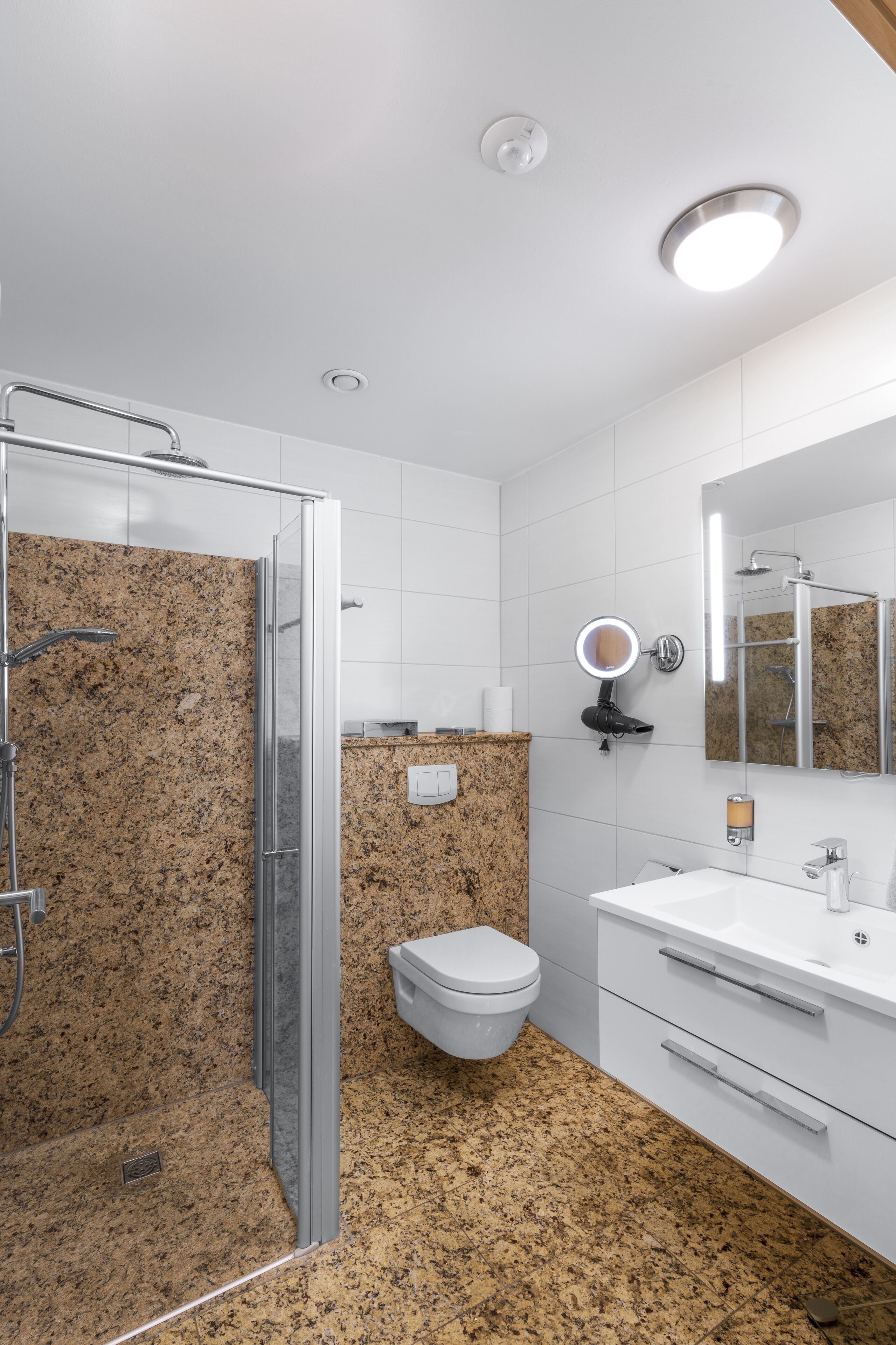 A modern bathroom with a glass shower enclosure, a white toilet, a sink with a mirror, and a vanity with drawers.