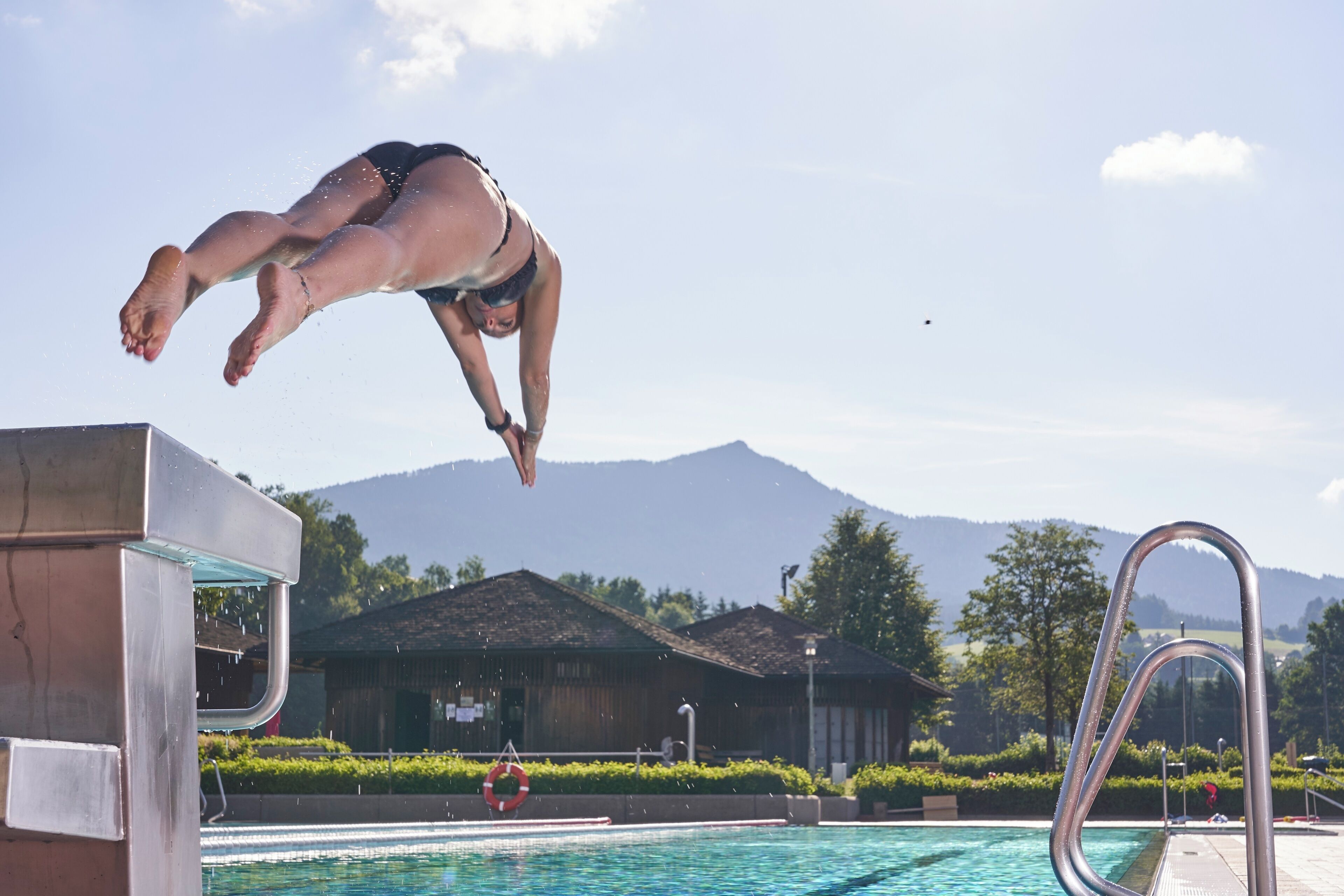A person diving into a pool with mountains in the background.