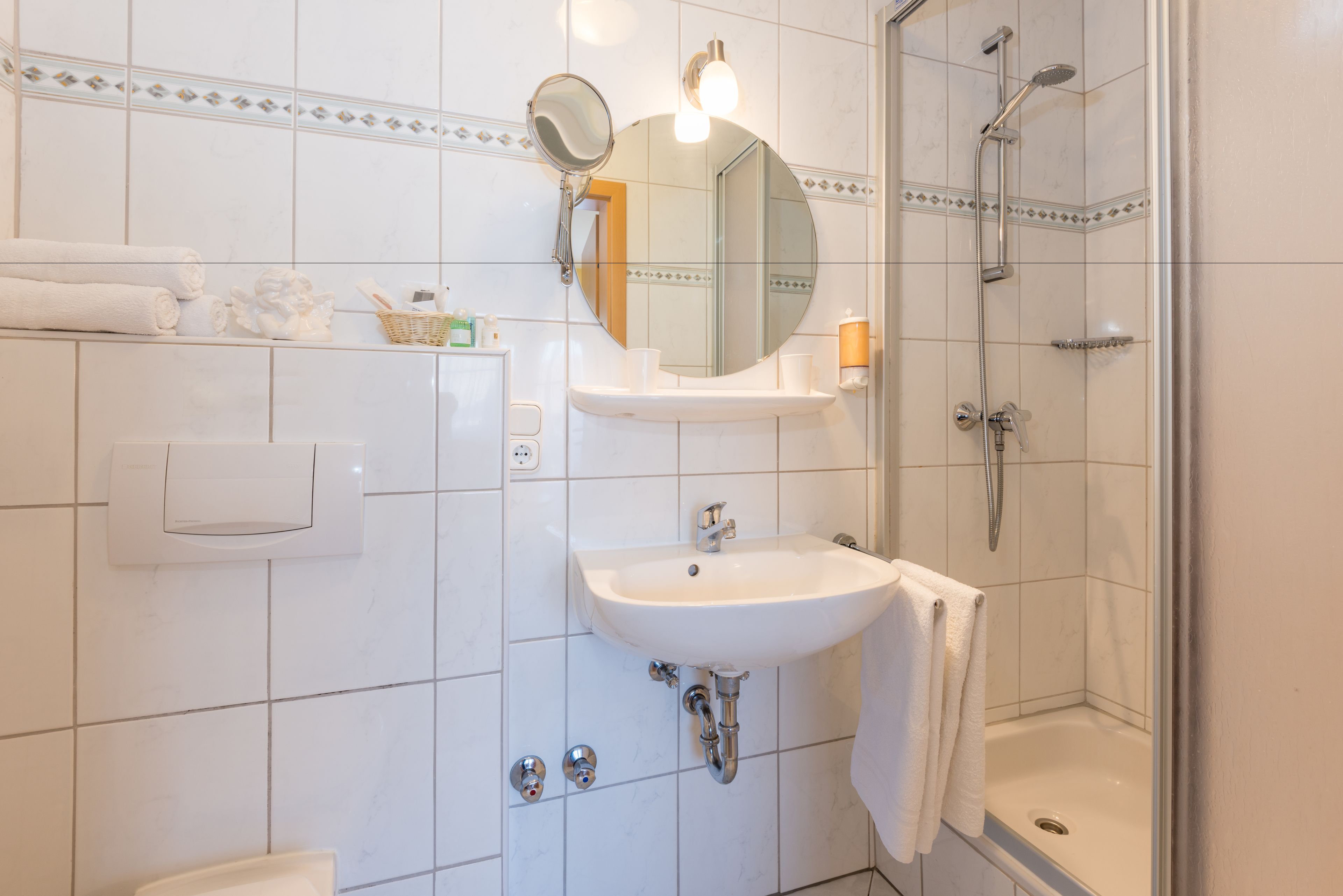 A bathroom with a sink, mirror, towel rack, shower, and a hand dryer.