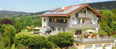 A two-story house with a balcony, solar panels, and a garden.