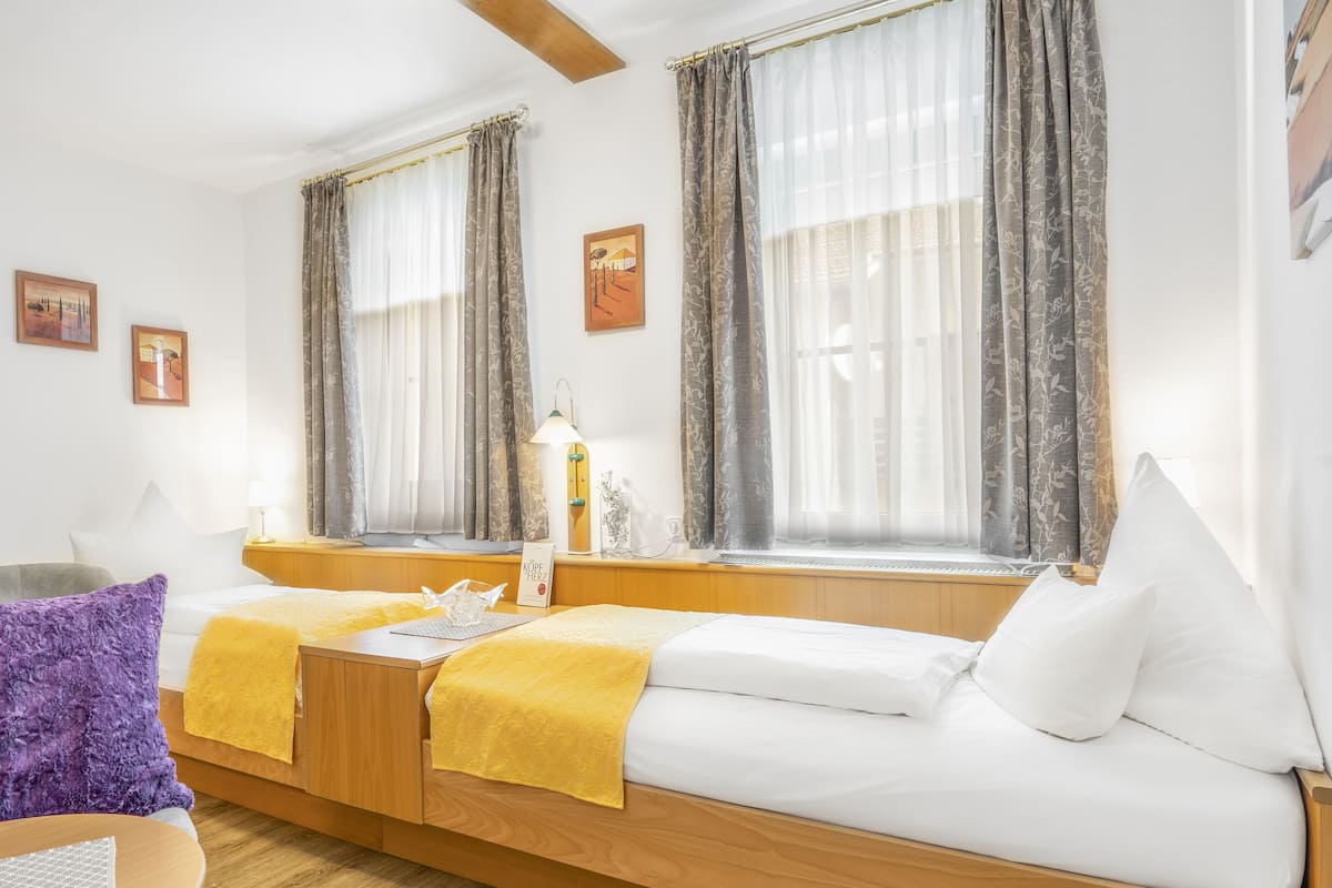 A hotel room with a wooden bed, a small table, and a window with curtains.