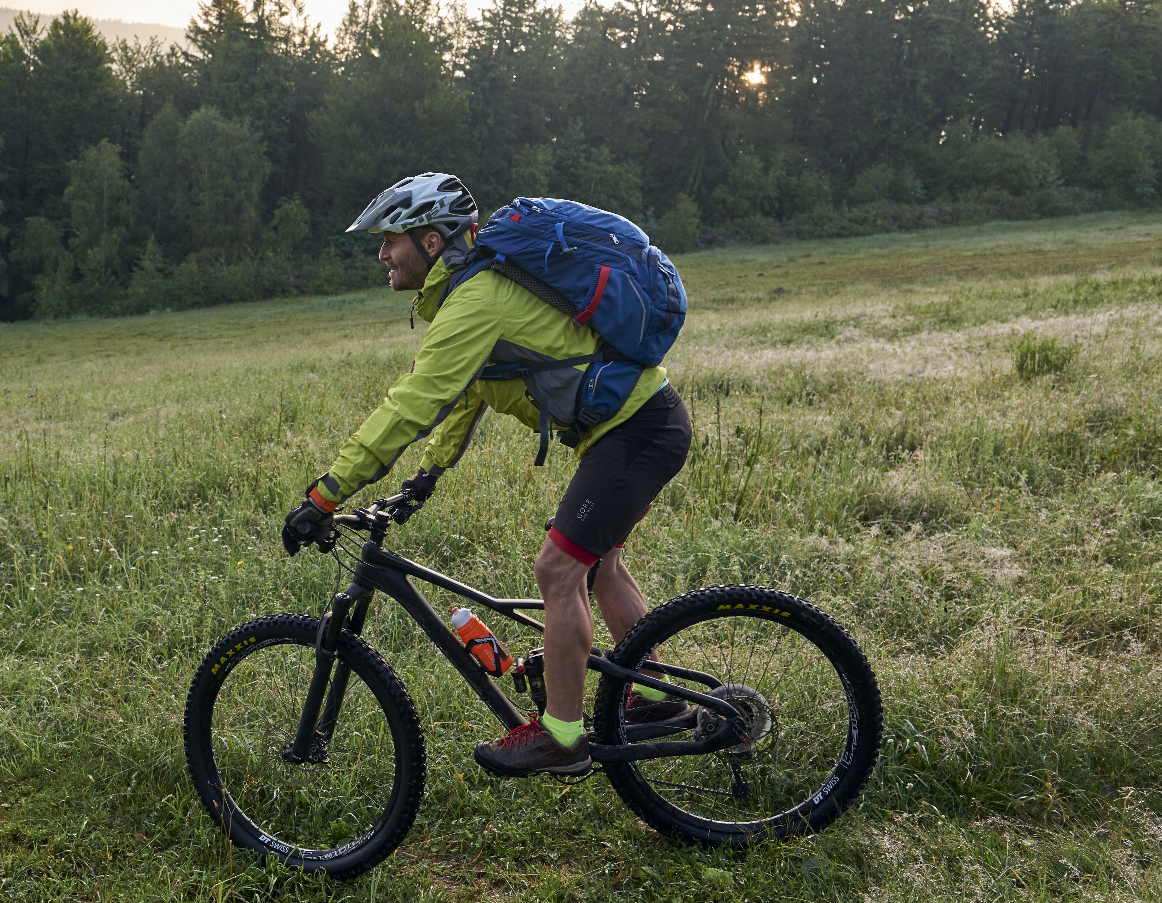 Una persona montando una bicicleta de montaña en un campo cubierto de hierba, con árboles al fondo.