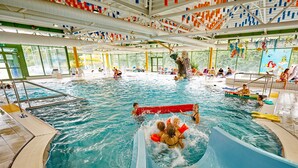 An indoor swimming pool with a slide, multiple lanes, and a lifeguard stand. - Hotel Rösslwirt (Lam)