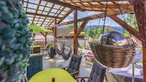 A covered outdoor seating area with wooden beams, wicker chairs, and hanging hammocks. - Hotel Rösslwirt (Lam)