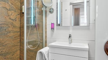 Un baño moderno con ducha envuelta en vidrio, un lavamanos blanco con espejo y piso de baldosas de mármol.
