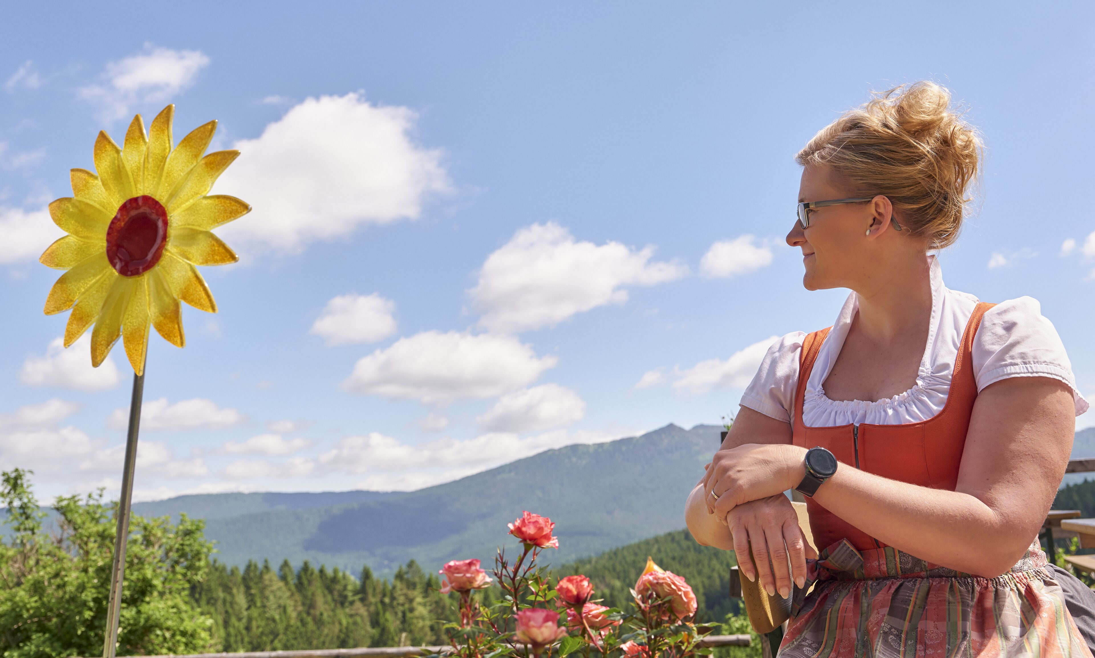 A person in traditional attire sitting outdoors with a mountain backdrop.