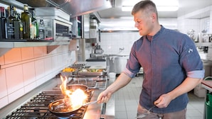 A chef cooking with a pan on a stove in a commercial kitchen. - Hotel Rösslwirt (Lam)