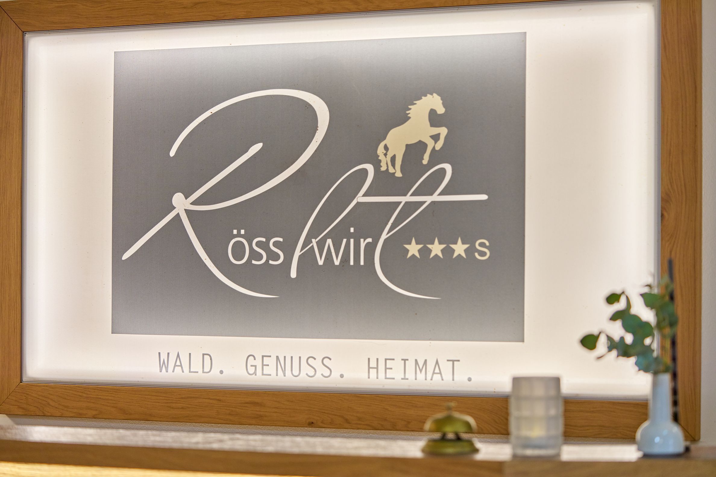 A framed sign with the text 'Rösswirt' and a horse silhouette, accompanied by the words 'Wald. Genuss. Heimat.'