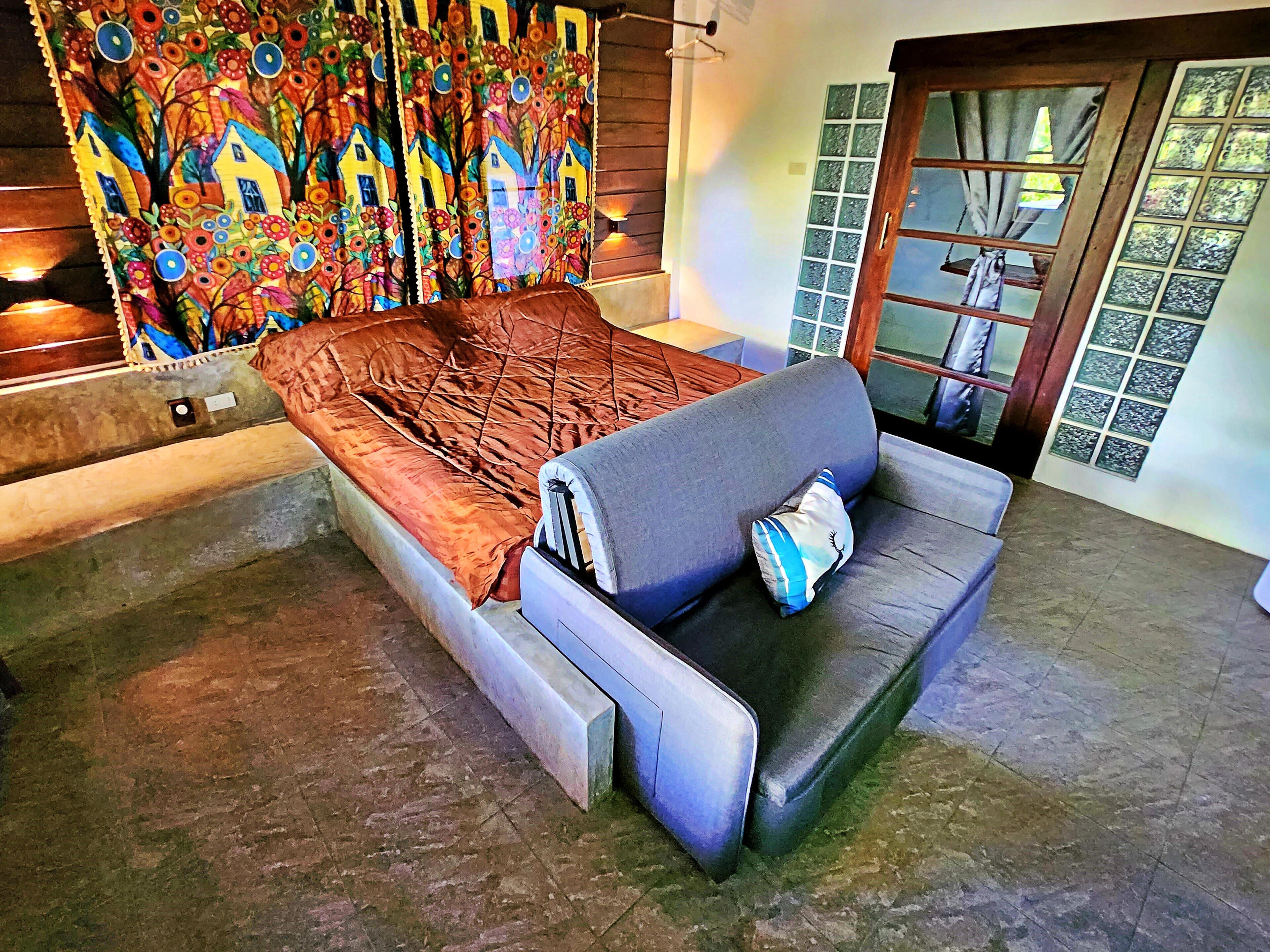 A room with a bed, a sofa, a colorful curtain, and a window with a view.