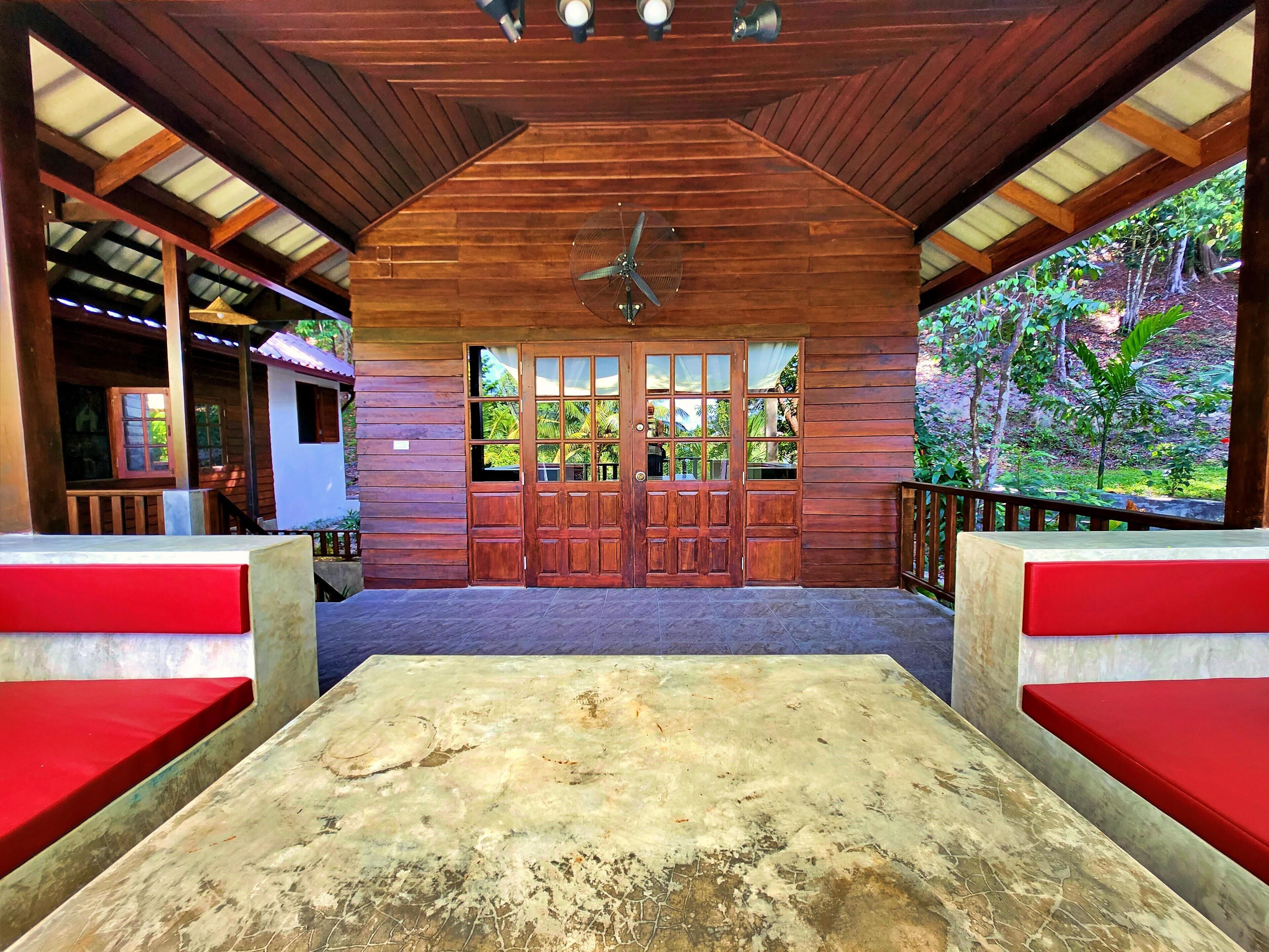 A wooden cabin with a large front door, a ceiling fan, and a view of a lush garden.