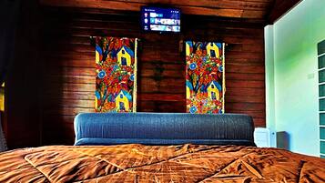 Quarto com cama, paredes de madeira, televisão na parede e cortinas coloridas.