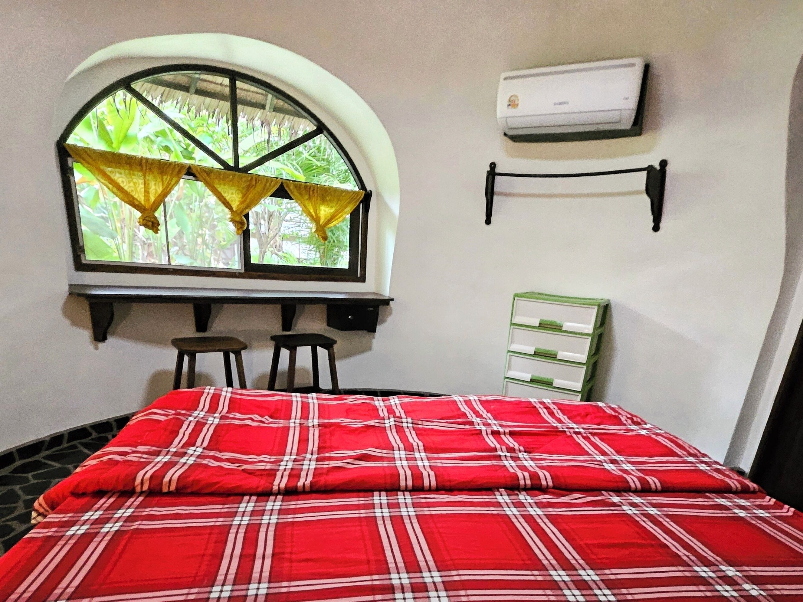A room with a bed, a window with curtains, a wall-mounted air conditioner, and a green storage unit.
