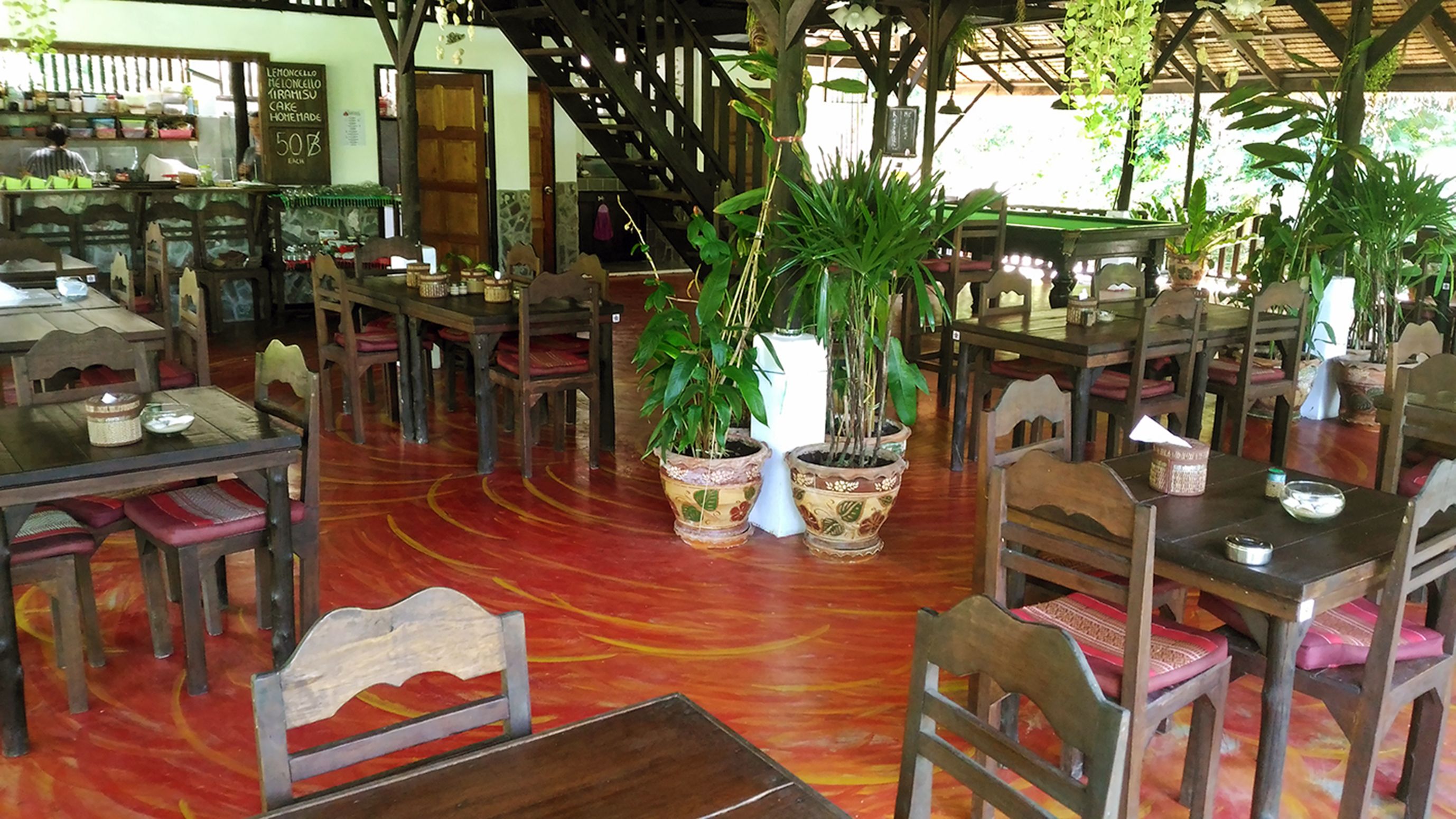 A restaurant with wooden furniture, potted plants, and a red patterned floor.