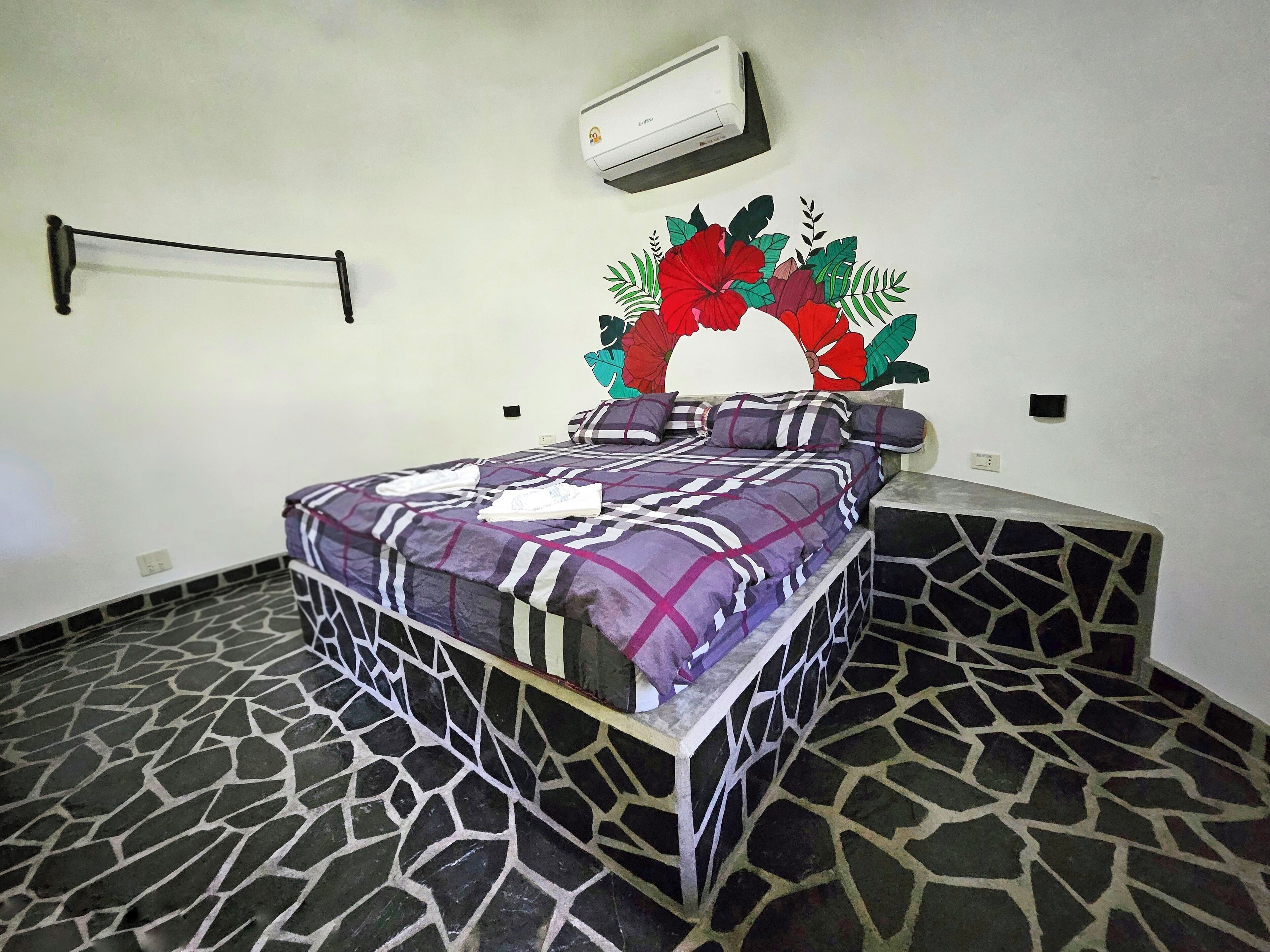 A bedroom with a bed, a wall-mounted air conditioner, and a decorative floral headboard.