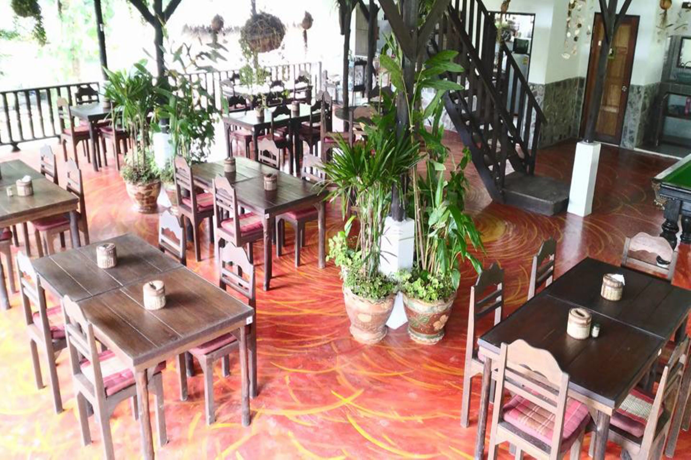 Un restaurante con mesas y sillas de madera, plantas en macetas y un piso de estampado rojo.