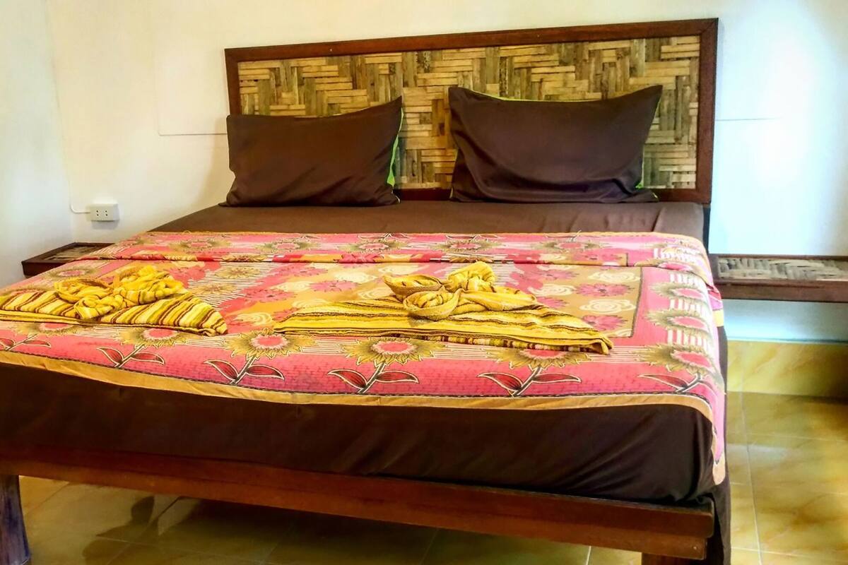Una cama con una colcha estampada, dos almohadas y una mesita de noche con una lámpara.