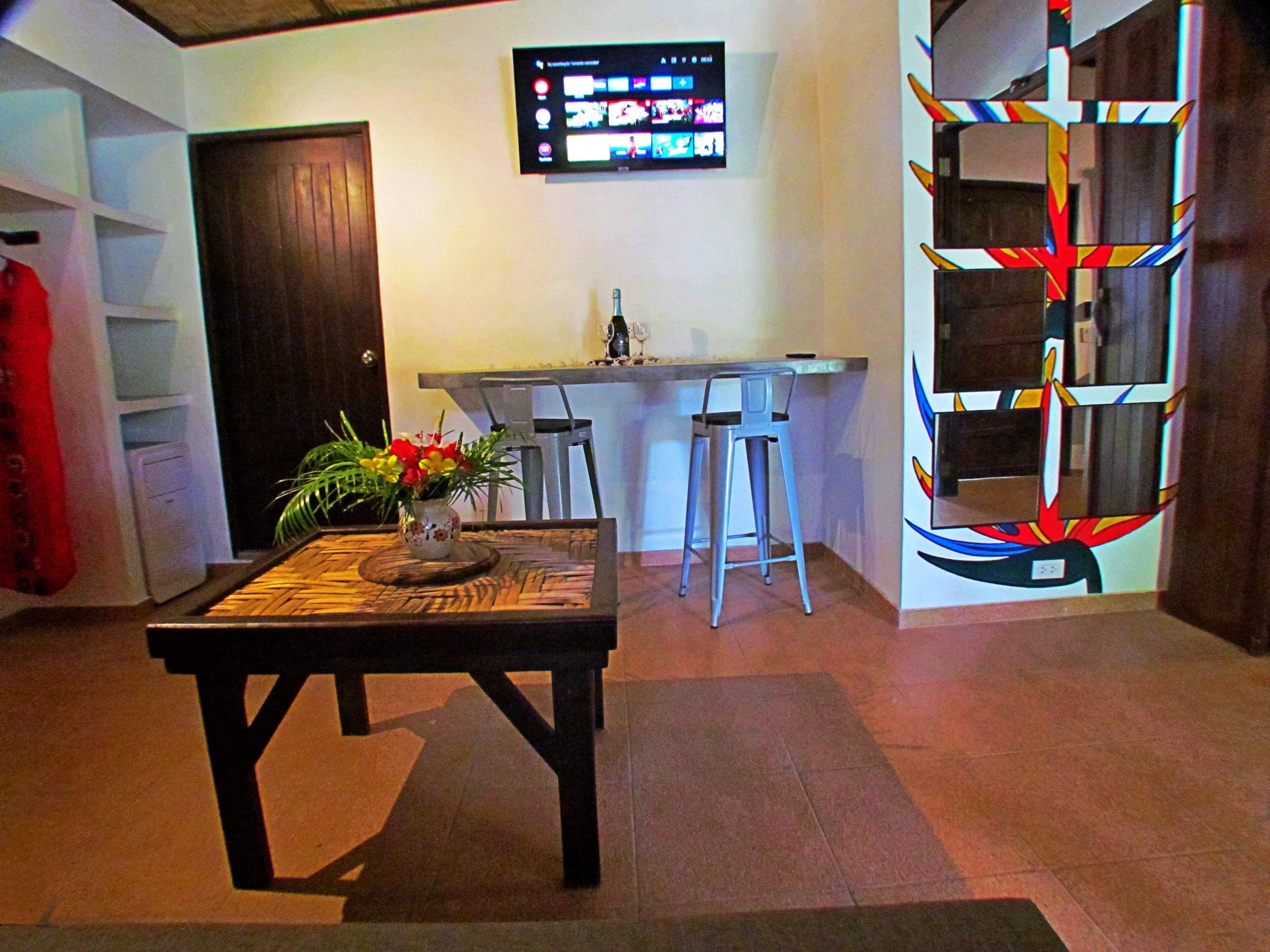 A room with a wooden table, a bar area, and a TV mounted on the wall.