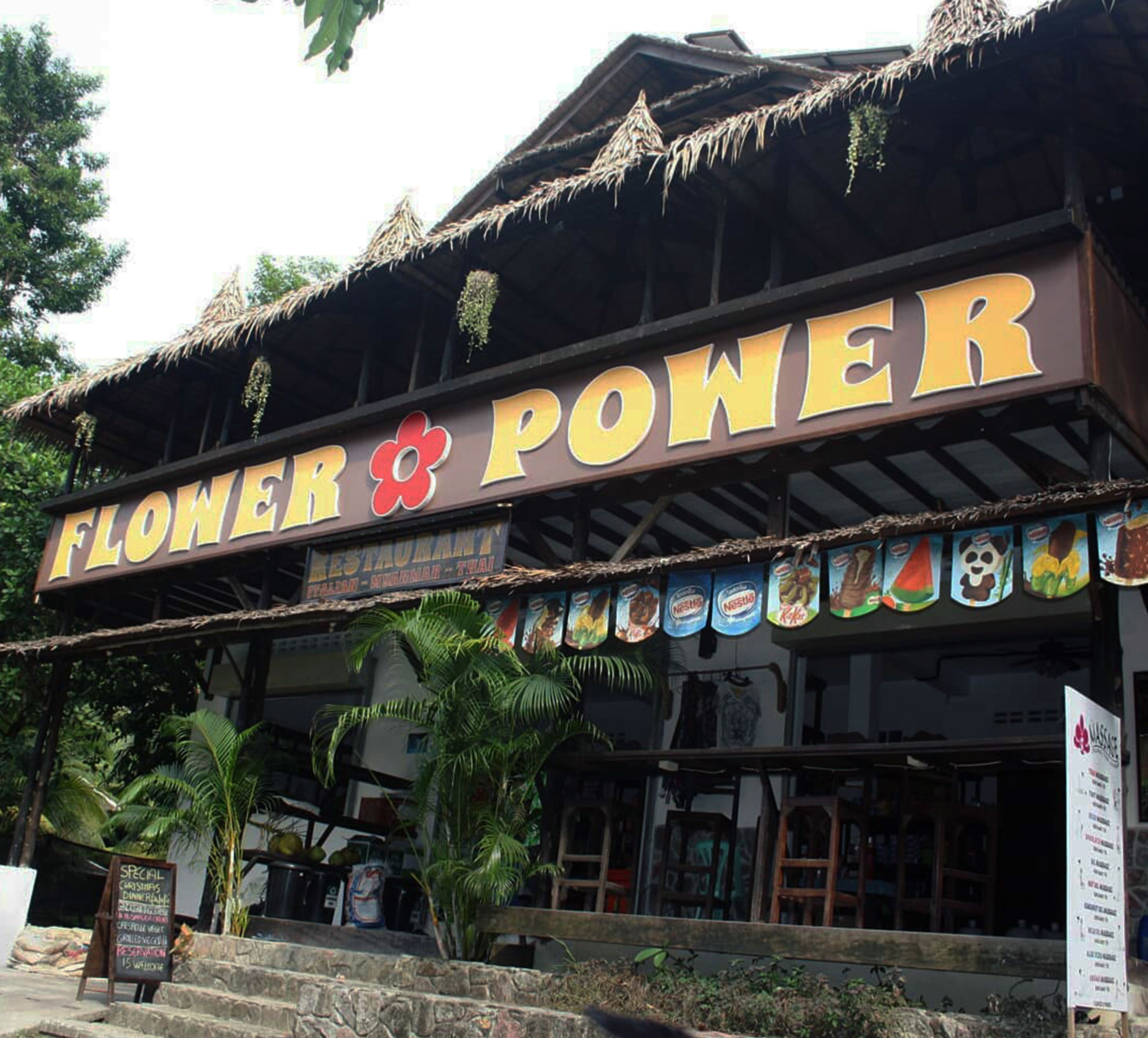 A restaurant named 'Flower & Power' with a tropical theme, including a thatched roof and various food items displayed outside.