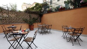 Un patio al aire libre con mesas y sillas, una planta en maceta y una barandilla adornada con flores.