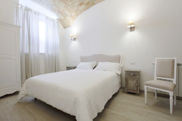 A bedroom with a bed, a chair, a nightstand, and a wardrobe. - Suite Maggiore (Rome)