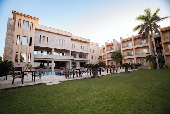 A multi-story hotel with outdoor seating, a swimming pool, and palm trees.
