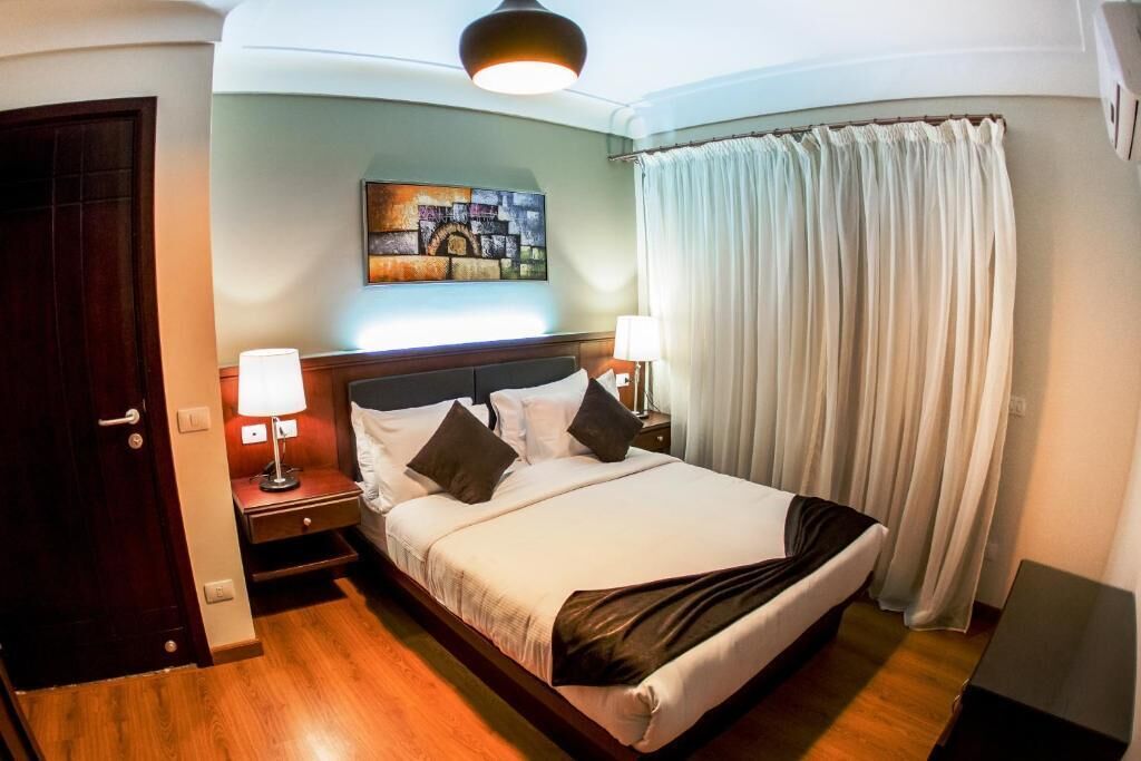 A hotel room with a bed, two bedside lamps, a painting on the wall, and a curtain.