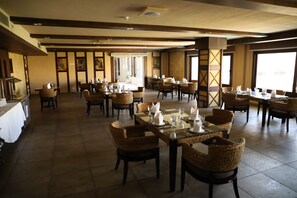 A spacious dining area with multiple tables and wicker chairs, featuring a high ceiling and large windows.
