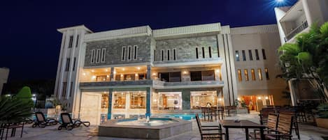 A two-story building with a swimming pool, outdoor seating, and a well-lit entrance.