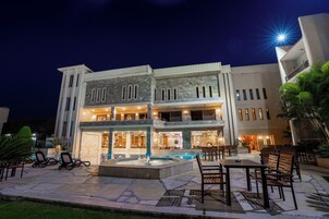 Un edificio de dos pisos con piscina, mobiliario exterior y una entrada bien iluminada.