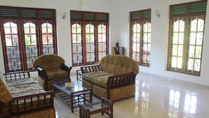 A spacious living room with traditional furniture, large windows with decorative grills, and a tiled floor. - Villa Comfort (Hikkaduwa)