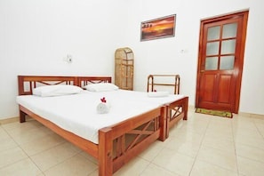 A neatly made bed with white linens, a wooden headboard, and a bedside table with a white cloth. There is a wooden bench against the wall, a door with glass panels, and a framed picture on the wall.